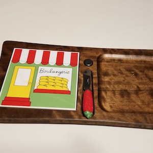 May include: Wooden serving tray with a built-in compartment and a decorative tile featuring a bakery scene. Includes a small knife with a red handle. The tile reads "Boulangerie".