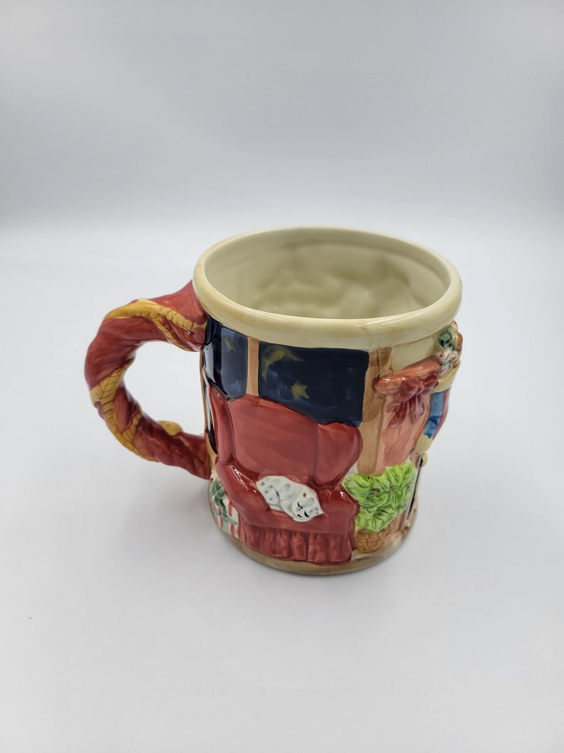 Pode incluir: Caneca de cer&acirc;mica decorativa com um design detalhado. A caneca apresenta uma al&ccedil;a vermelha com detalhes dourados e retrata uma sala com um sof&aacute; vermelho, um gato dormindo e uma janela com um c&eacute;u estrelado. Um item decorativo.