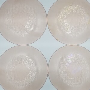 May include: Four pale pink glass plates with a floral design in the center. The plates have a slightly raised rim and a delicate, embossed pattern of flowers and leaves. The plates are arranged in a square formation.