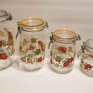 May include: Four clear glass jars with hinged lids, varying in size. Each jar is decorated with a colorful pattern of vegetables, including tomatoes, mushrooms, and onions. The jars are designed for food storage.