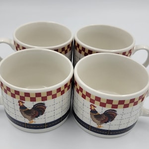 May include: Four white ceramic mugs with a rooster design. Each mug has a cream-colored interior, a handle, and a decorative band with a red and tan checkered pattern. A rooster illustration is on the front of each mug.
