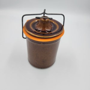 May include: A brown ceramic jar with a lid and a wire handle. The lid has an orange rubber seal.