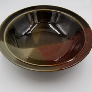 May include: A ceramic oval serving bowl with a glossy finish. The bowl features a color-blocked design with sections of dark brown, olive green, and reddish-brown. The rim is a darker shade of brown.