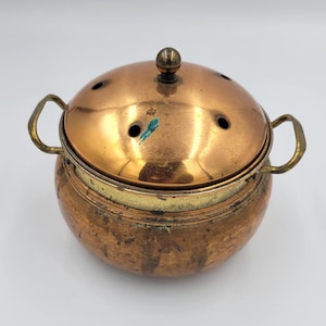 Peut inclure: Un brûleur d'encens en cuivre avec un couvercle en forme de dôme percé de petits trous. Il possède deux poignées et une bande de couleur laiton au milieu. Le couvercle est surmonté d'un petit bouton. Design vintage.