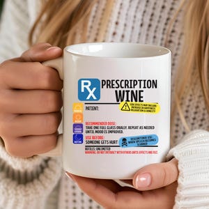 Puede incluir: Una taza de cer&aacute;mica blanca con un dise&ntilde;o gr&aacute;fico que imita una etiqueta de receta m&eacute;dica con el texto Prescription Wine. El dise&ntilde;o incluye iconos para ma&ntilde;ana, mediod&iacute;a, tarde y noche, junto con instrucciones y advertencias en negro, azul y amarillo.