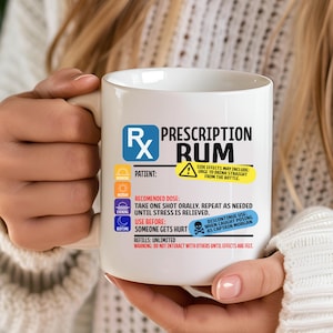 Puede incluir: Una taza de cer&aacute;mica blanca con un dise&ntilde;o gr&aacute;fico que imita una etiqueta de receta m&eacute;dica con el texto Prescription Rum. El dise&ntilde;o incluye iconos para ma&ntilde;ana, mediod&iacute;a, tarde y noche, junto con instrucciones y advertencias impresas en texto negro, azul, amarillo y rojo.