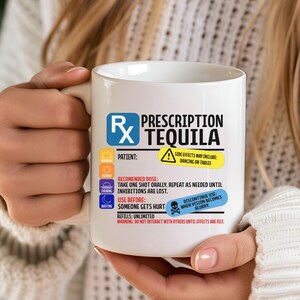 Puede incluir: Una taza de cer&aacute;mica blanca con un gr&aacute;fico de etiqueta de receta que dice Prescription Tequila. El dise&ntilde;o incluye iconos para ma&ntilde;ana, mediod&iacute;a, tarde y noche, junto con texto sobre efectos secundarios, dosis y advertencias en negro, azul y amarillo.