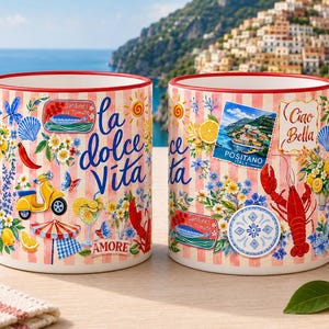 May include: Two ceramic mugs with red handles and rims. The mugs feature a design with Italian imagery, including a yellow scooter, lobster, and the words "la dolce Vita" and "Ciao Bella". The background is a pink and white striped pattern.