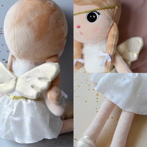 May include: A plush angel doll with blonde hair, white wings, and a white tulle skirt with gold glitter. The doll is wearing a gold headband and has a white fur trim around the neck.