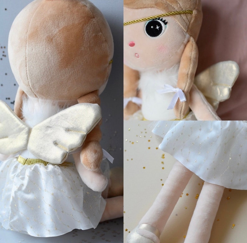 May include: A plush angel doll with blonde hair, white wings, and a white tulle skirt with gold glitter. The doll is wearing a gold headband and has a white fur trim around the neck.