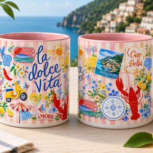 May include: Two ceramic mugs with pink handles and rims. The mugs are decorated with Italian-themed illustrations, including the words "la dolce Vita" and "Ciao Bella", along with images of a scooter, lobster, and Positano.