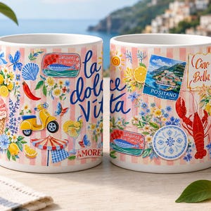 May include: Two white ceramic mugs with a colorful Italian-themed design. The mugs feature illustrations of lemons, a red lobster, a yellow scooter, and the words "la dolce Vita" and "Ciao Bella". The mugs have a pink and white striped background.