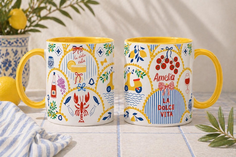 Puede incluir: Dos tazas de cer&aacute;mica blanca con asas e interiores amarillos. Las tazas presentan coloridas ilustraciones de tem&aacute;tica italiana, incluyendo limones, un scooter y las palabras "La Dolce Vita" y "Amelia".