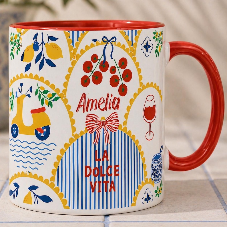 Puede incluir: Taza de cer&aacute;mica blanca con interior y asa rojos. La taza presenta un dise&ntilde;o colorido con limones, un scooter amarillo, cerezas, un lazo rojo y los textos "Amelia" y "LA DOLCE VITA".