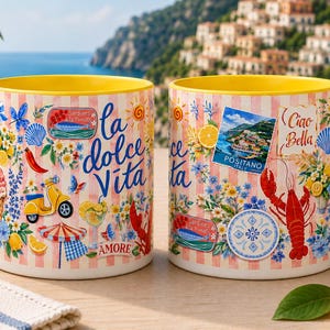 May include: Two ceramic mugs with yellow handles and interiors. The mugs feature a design with Italian imagery, including a lobster, scooter, and the words "La Dolce Vita" and "Ciao Bella". The background has a pink and white striped pattern.