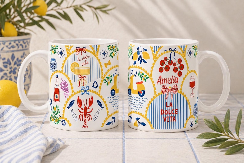 Puede incluir: Dos tazas de cer&aacute;mica blanca con dise&ntilde;os italianos coloridos. Una taza presenta una langosta, peces y el texto "la dolce vita". La otra taza tiene un scooter, cerezas y el nombre "Amelia". Ambas tazas tienen un asa curva.