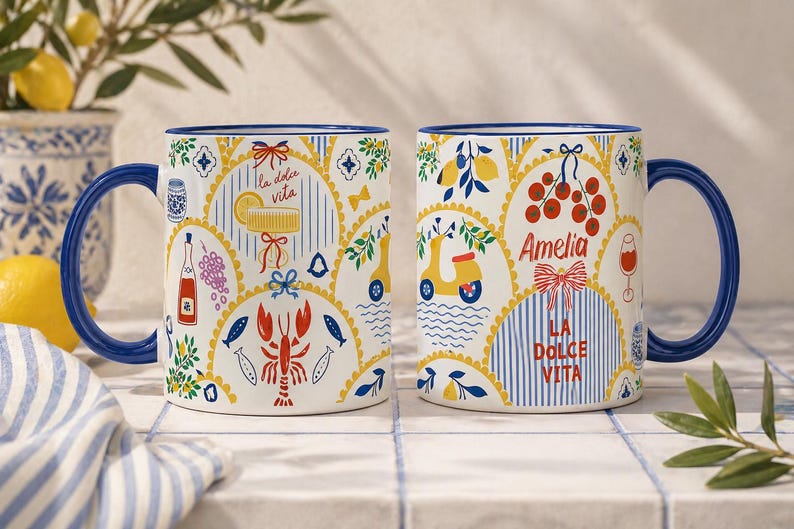 Puede incluir: Dos tazas de cer&aacute;mica blanca con asas y bordes azules. Las tazas presentan ilustraciones coloridas de limones, un scooter y el texto "La Dolce Vita". Una taza tiene el nombre "Amelia".