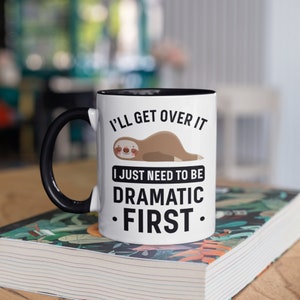 Puede incluir: Taza de cerámica blanca con asa e interior negros. La taza presenta una ilustración de perezoso y el texto "I'll get over it, I just need to be dramatic first."
