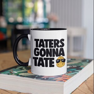May include: White ceramic mug with a black rim and handle. The mug has a black graphic that says "Taters Gonna Tate" with a cartoon potato wearing sunglasses.