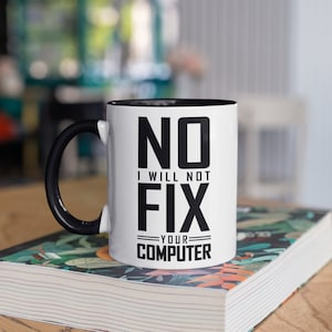 Puede incluir: Taza de cerámica blanca con interior y asa negros. La taza presenta el texto "NO I WILL NOT FIX YOUR COMPUTER" en letras negras en negrita. La taza está sobre un libro con un diseño floral.