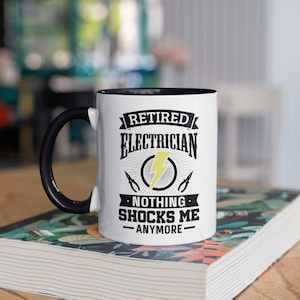 May include: White coffee mug with a black rim and handle. The mug has a black and white graphic that says "Retired Electrician. Nothing shocks me anymore." with a lightning bolt and a pair of pliers.
