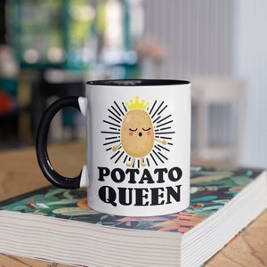 May include: White ceramic mug with a black handle and interior. The mug features a cartoon potato character wearing a gold crown, surrounded by radiating lines, and the words "POTATO QUEEN" in bold black letters.