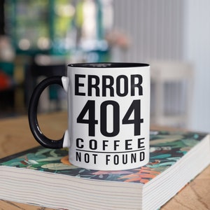 Może przedstawiać: Biały kubek do kawy z czarnym uchwytem i czarnym rantem. Kubek ma czarny napis "ERROR 404 COFFEE NOT FOUND".
