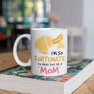 May include: White ceramic mug with a fortune cookie graphic and the text "I'M SO FORTUNATE TO HAVE YOU AS A MOM." The fortune cookie is yellow with a banner that says "i love u."