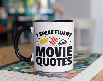 May include: White coffee mug with a black handle. The mug has a black rim and the text "I speak fluent movie quotes" in black lettering. There are illustrations of a movie ticket, popcorn, and 3D glasses.