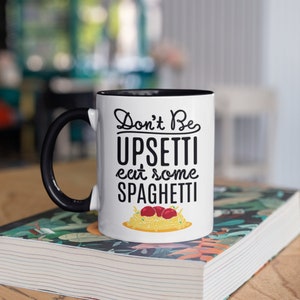 May include: White ceramic mug with a black rim and handle. The mug has a black graphic that says "Don't Be Upsetti eat some SPAGHETTI" with a cartoon image of spaghetti and meatballs.