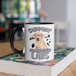 Puede incluir: Taza de cerámica blanca con interior y asa negros. La taza presenta un Labrador Retriever con gafas, rodeado de iconos informáticos y el texto "SUPPORT COMPUTER LABS" en gris.