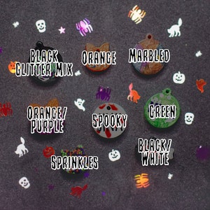 May include: Assortment of Halloween-themed cat collar charms.  The charms are made of resin and feature various designs, including a black glitter mix, orange, marbled, orange and purple, spooky, green, sprinkles, and black and white.