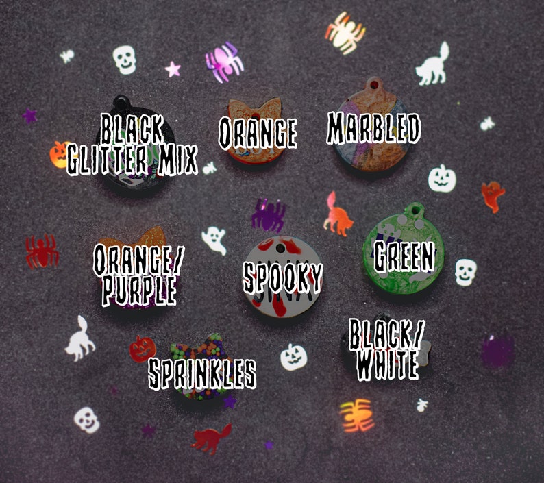 May include: Assortment of Halloween-themed cat collar charms.  The charms are made of resin and feature various designs, including a black glitter mix, orange, marbled, orange and purple, spooky, green, sprinkles, and black and white.