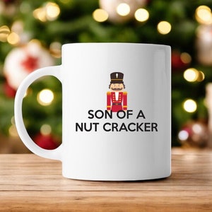 May include: White ceramic coffee mug with a black and red illustration of a nutcracker and the text "Son of a Nutcracker".
