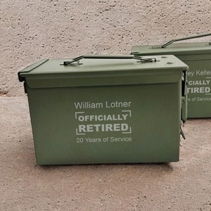 May include: Two green metal ammo boxes with white text. The top box says "William Lotner Officially Retired 20 Years of Service". The bottom box says "ey Keller Officially Tired Years of Service".