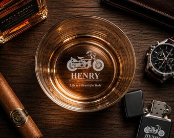 May include: A clear glass whiskey tumbler featuring an etched motorcycle graphic, the name HENRY, and the text Life is a Beautiful Ride. A matching black metal lighter with the same motorcycle design and text is positioned next to the glass.