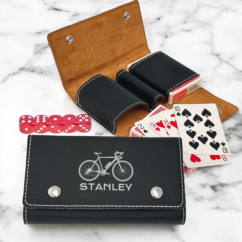 May include: Black leather card and dice case with a white bicycle design and the name "STANLEY" engraved on the front. The case has two slots for decks of cards and a small compartment for dice.