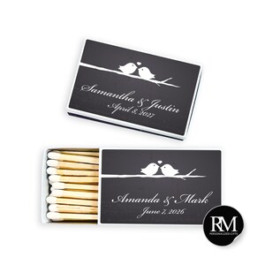 May include: Two rectangular matchboxes with a black chalkboard-style finish. Each features a white graphic of two birds on a branch with a heart above them. One box is closed, the other open showing wooden matches. Text reads Samantha & Justin April 8, 2027 and Amanda & Mark June 7, 2026.