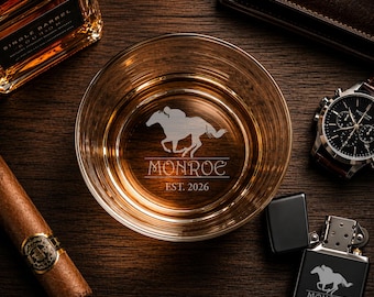 May include: A clear glass whiskey tumbler featuring an etched design of a horse and jockey with the text MONROE EST. 2026. A matching black metal lighter with the same horse and jockey graphic and text is positioned next to the glass.