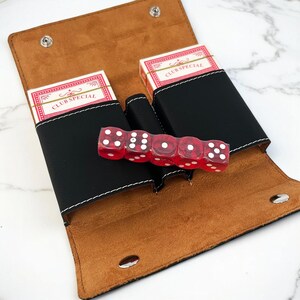 May include: A black leather case with two decks of cards and red dice. The case has a brown suede lining and white stitching. The cards are labeled "Club Special".