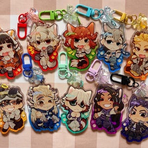 Könnte beinhalten: Eine Sammlung von elf Acryl-Schlüsselanhängern mit Chibi-Anime-Figuren mit Tierohren. Jeder Schlüsselanhänger verfügt über einen farbigen Kunststoff-Karabinerverschluss und einen kleinen dekorativen Anhänger mit verschiedenen Charakterdesigns.