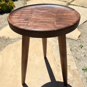 May include: A round wooden side table with a dark brown finish and three legs. The table top has a natural wood grain pattern.