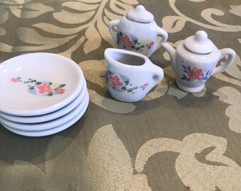 May include: A miniature tea set with a white teapot, creamer, sugar bowl, and four plates. The set is decorated with pink and green floral designs.