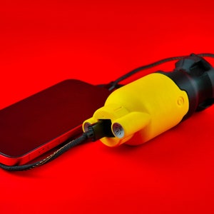 Puede incluir: Un cargador de teléfono portátil amarillo y negro con un cable negro conectado a un teléfono inteligente negro.
