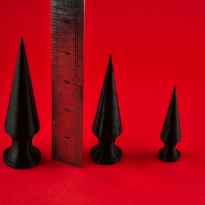 May include: Three black, pointed, cone-shaped objects of varying sizes, with a ruler for scale.