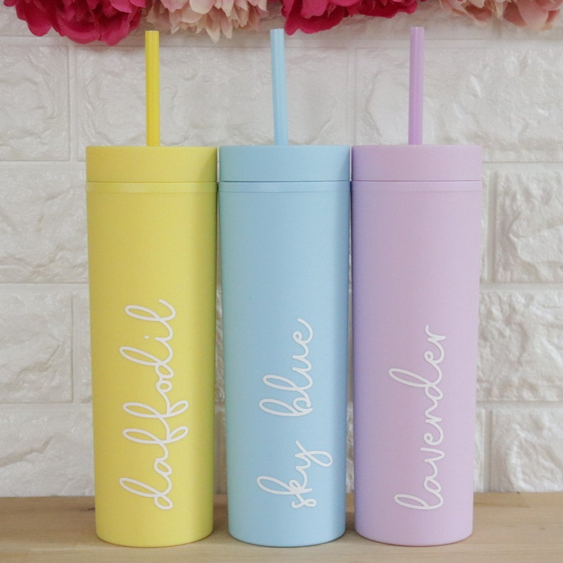 May include: Three tall, reusable tumblers with matching straws. The tumblers are yellow, light blue, and lavender. Each tumbler has a different color and a white inscription: "daffodil", "sky blue", and "lavender".