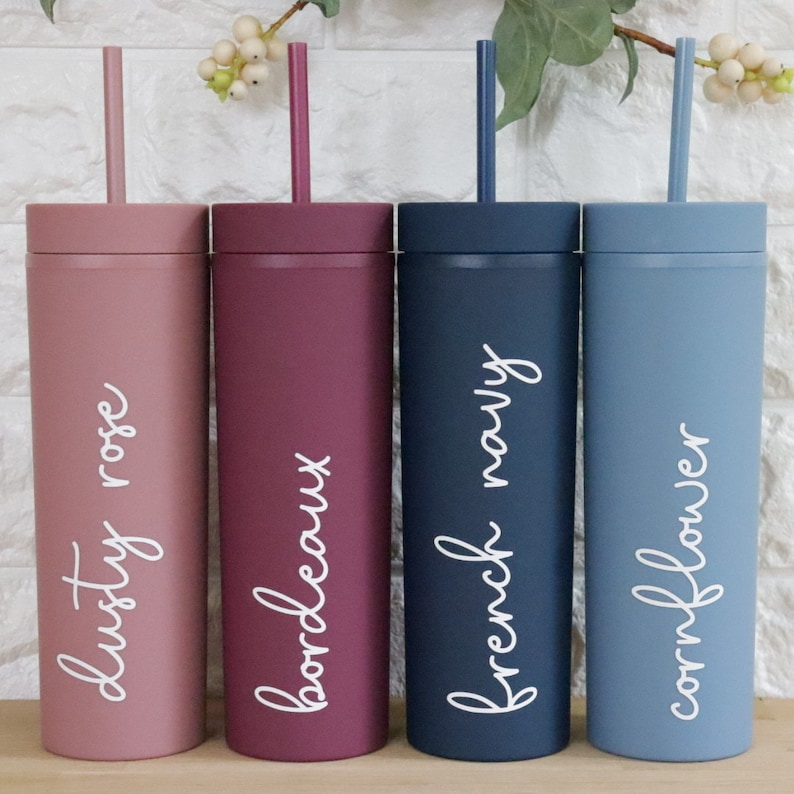 May include: Four tall, reusable tumblers with straws. The tumblers are in dusty rose, burgundy, navy blue, and light blue. Each tumbler has a different color and a white handwritten name on the side: "dusty rose", "bordeaux", "french navy", and "cornflower".