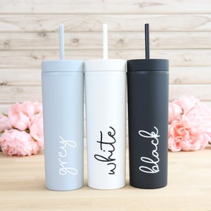 May include: Three stainless steel tumblers with lids and straws. The tumblers are grey, white, and black. Each tumbler has the color name written on it in white.
