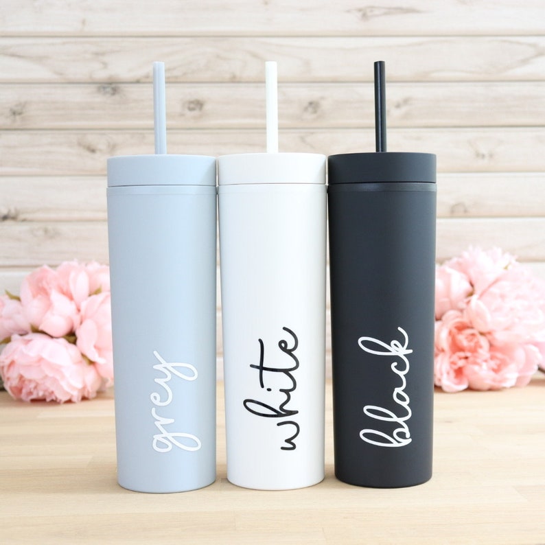 May include: Three stainless steel tumblers with lids and straws. The tumblers are grey, white, and black. Each tumbler has the color name written on it in white.