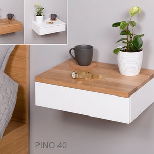May include: White floating nightstand with a drawer and a wood top. The nightstand has a plant in a white pot and a watch on the top. The text "PINO 40" is on the bottom of the image.